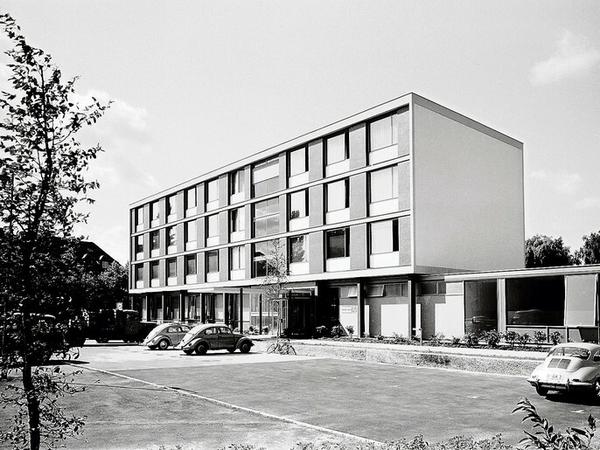 Ein Universitätsinstitut im Stil der frühen 1960er Jahren mit geparkten VW-Käfern davor.