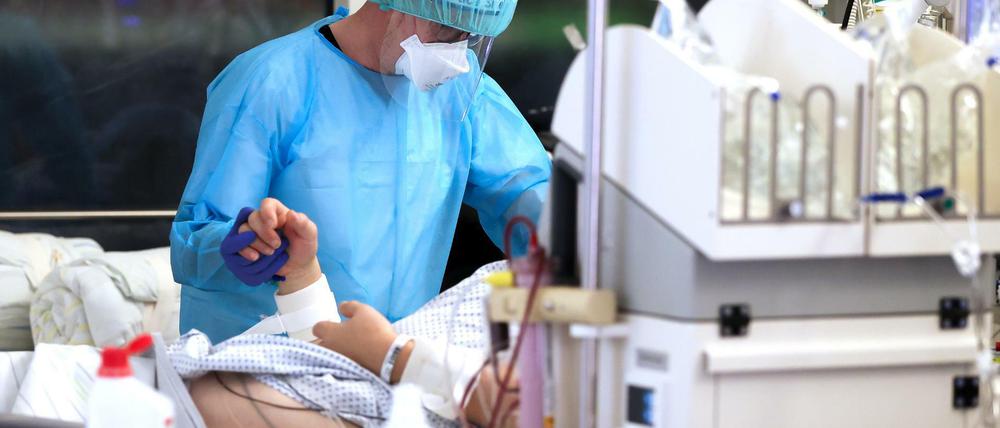 Ein Facharzt versorgt einen Covid-19-Patienten auf der Intensivstation der Leipziger Uniklinik und hält dessen Hand.