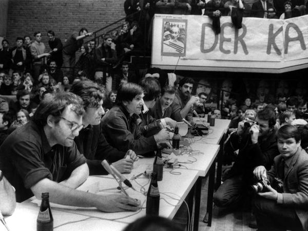 Studenten sitzen bei einer Konferenz an einem Podium, in der Mitte sitzt Rudi Dutschke.