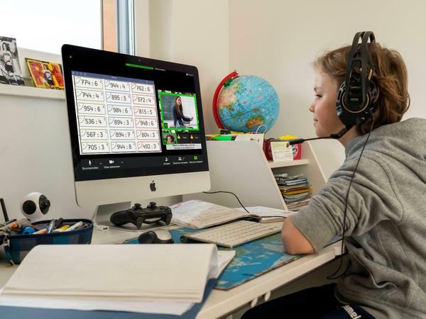 Ein Junge sitzt an seinem Schreibtisch am PC, dabei trägt er Kopfhörer.
