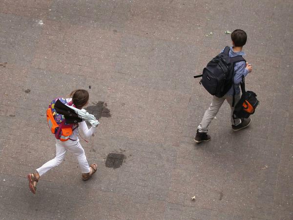 Ein junge und ein Mädchen mit Schultaschen auf den Rücken gehen quer über einen Schulhof.