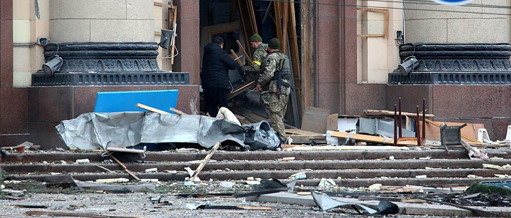 Ukrainische Soldaten und ein Zivilist hantieren vor einem Verwaltungsgebäude in Charkiv mit zerstörten Möbeln.