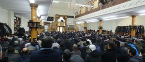 Betende Männer knien in einer überfüllten Moschee und blicken nach vorne zum Imam.