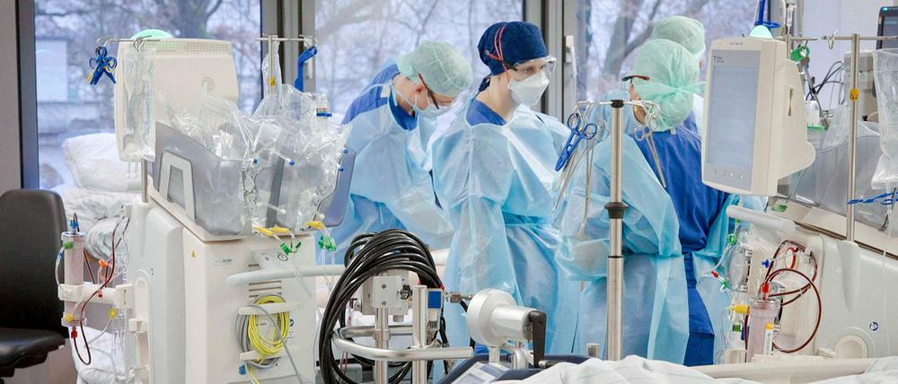Vier Intensivmediziner:innen stehen in Schutzanzügen an einem Krankenbett.
