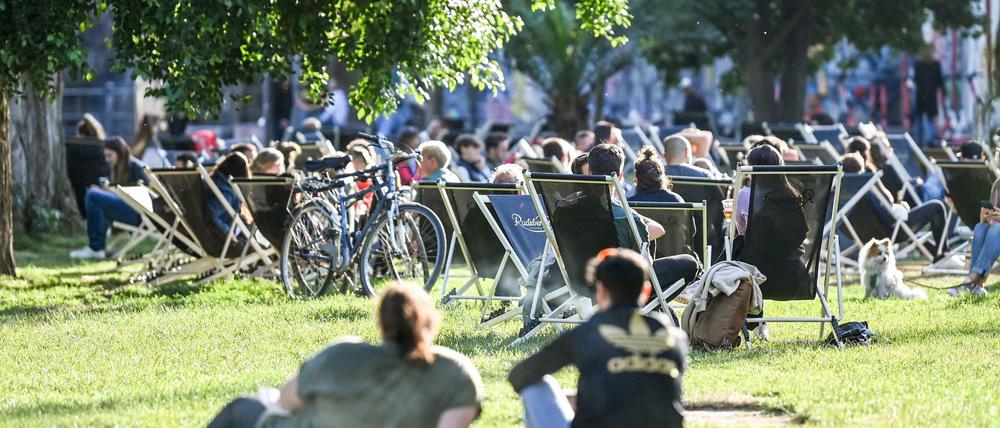 Zahlreiche Menschen sitzen auf Liegestühlen und auf der Wiese in der untergehenden Sonne am Sonntagabend im James-Simon-Park.