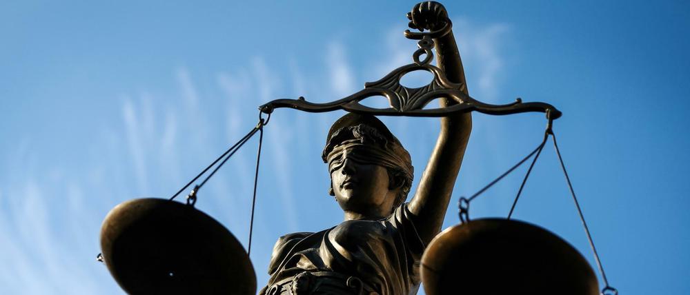 Eine Justitia-Statute, die eine Waage in der Hand hält, ist schräg von unten gegen den blauen Himmel fotografiert.