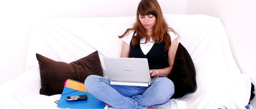 Eine junge Frau sitzt auf einem Sofa und arbeitet auf dem Laptop.