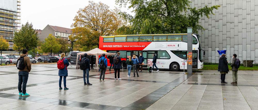 Ein rot-weißer Doppeldeckerbus steht vor einem Universitätsgebäude, davor hat sich eine Schlage von Studierenden gebildet.