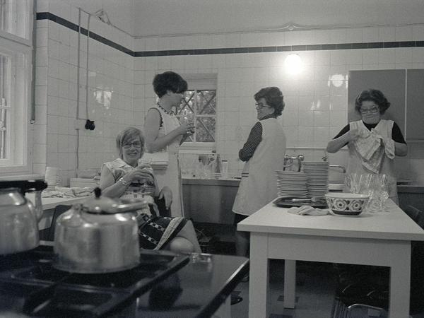 Zwei weibliche Gäste des Klubhauses unterhalten sich in der Küche mit zwei Mitarbeiterinnen, die abwaschen, beziehungsweise abtrocknen.