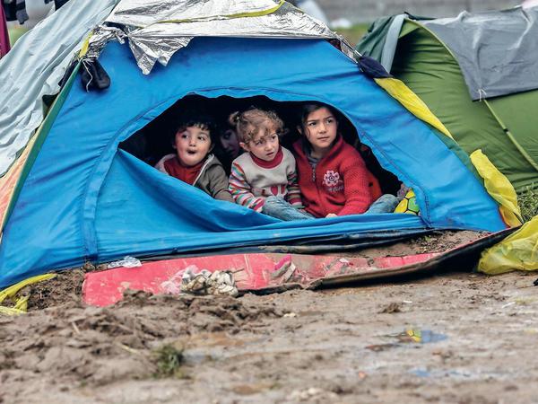 Drei kleine Kinder im Alter von etwa drei bis sechs Jahren sitzen in einem Flüchtlingslager in einem Igluzelt.