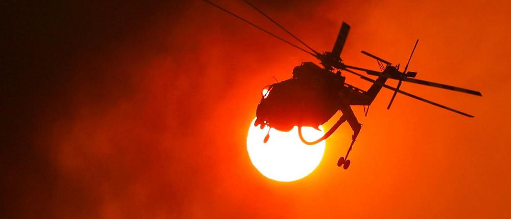 Ein Feuerwehrhubschrauber fliegt in Griechenland vor der Sonne zu einem Waldbrand.