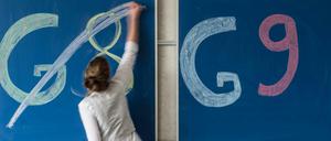 Eine Frau streicht den Schriftzug G8 auf einer Tafel durch, daneben ist eine Tafel mit dem Schriftzug G9 zu sehen.